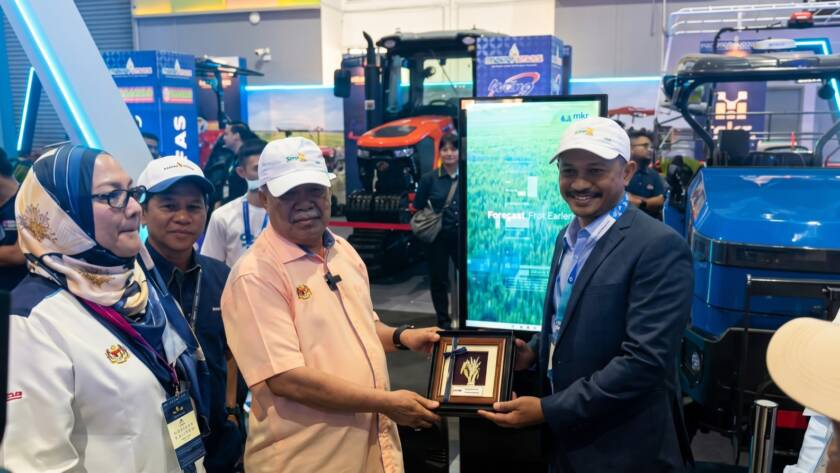 A souvenir is presented at the MKR booth as SemaiSens runs on screen at MAHA 2026