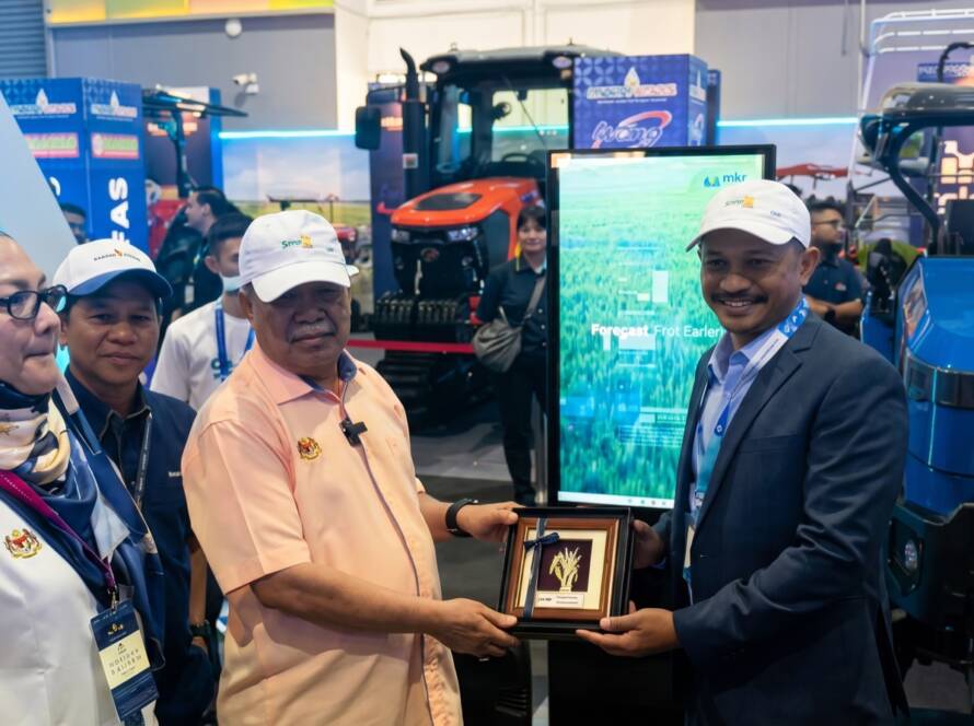 A souvenir is presented at the MKR booth as SemaiSens runs on screen at MAHA 2026